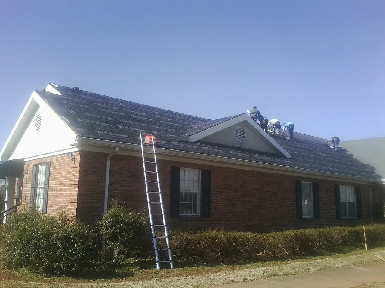 Crew tearing shingles off a brick ranch roof with a ladder set — Metal Roof Repair work by our crew in Slate Run
