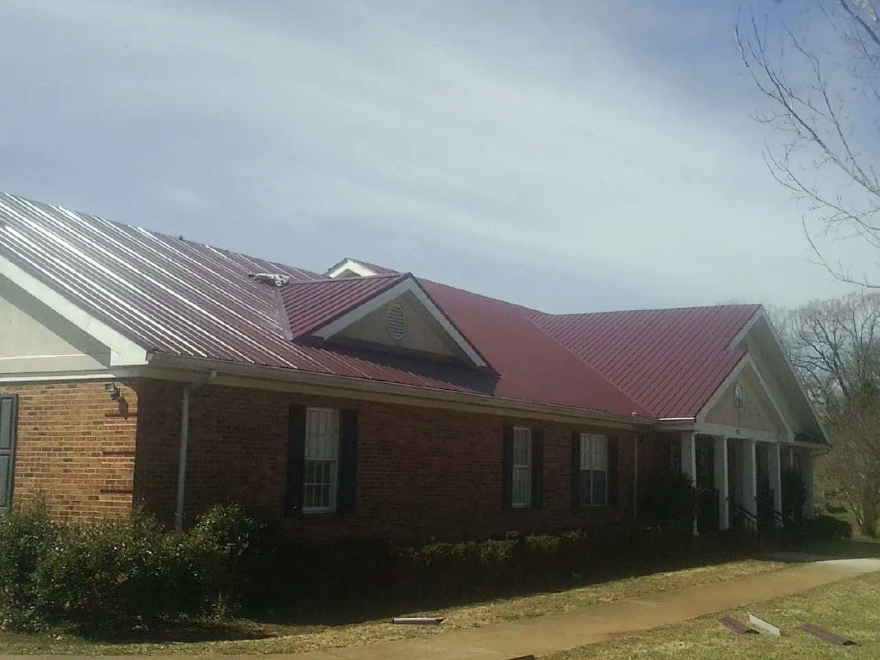 Red metal roof with gabled entries on a long brick building, from a Hail Damage Roof Repair job in Slate Run