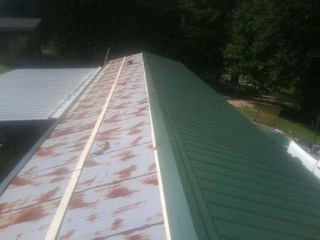 Old rusted panels beside newly installed green metal roofing — Wind Damage Roof Repair by Roofing Brothers in Slate Run