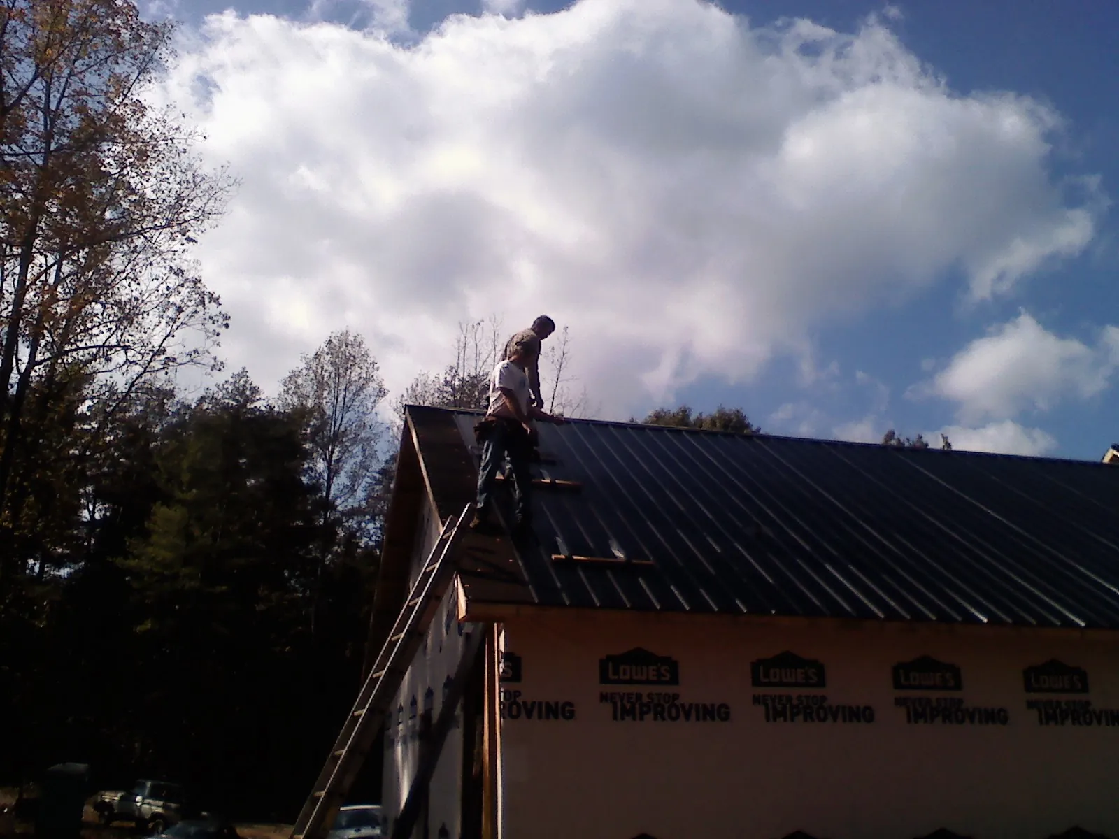 Roofer fastening dark metal panels high against a cloudy sky, from a Roof Inspection job in Slate Run