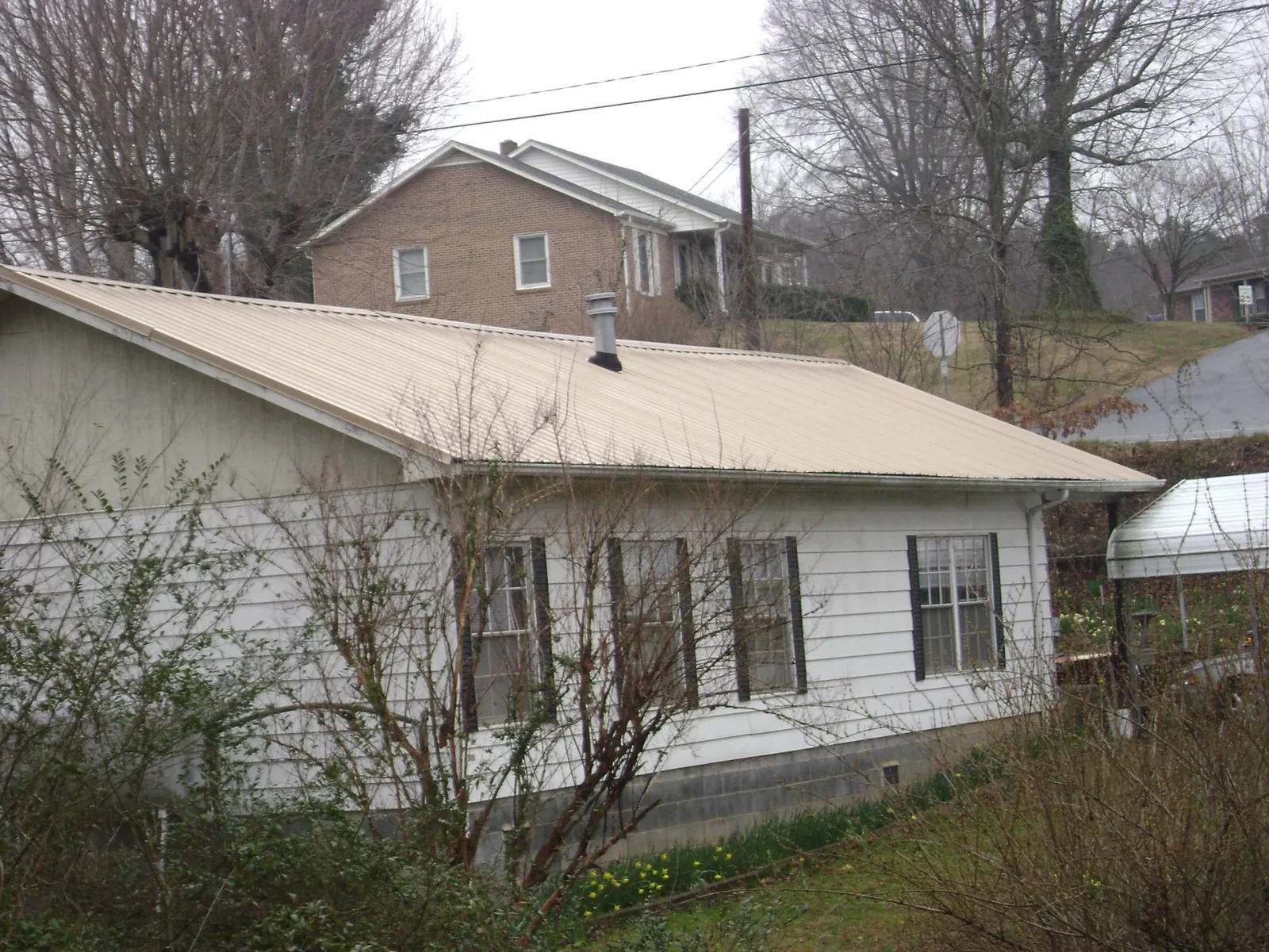 Tan metal roof on a white sided house set into a hillside — Commercial Roofing by Roofing Brothers in Slate Run